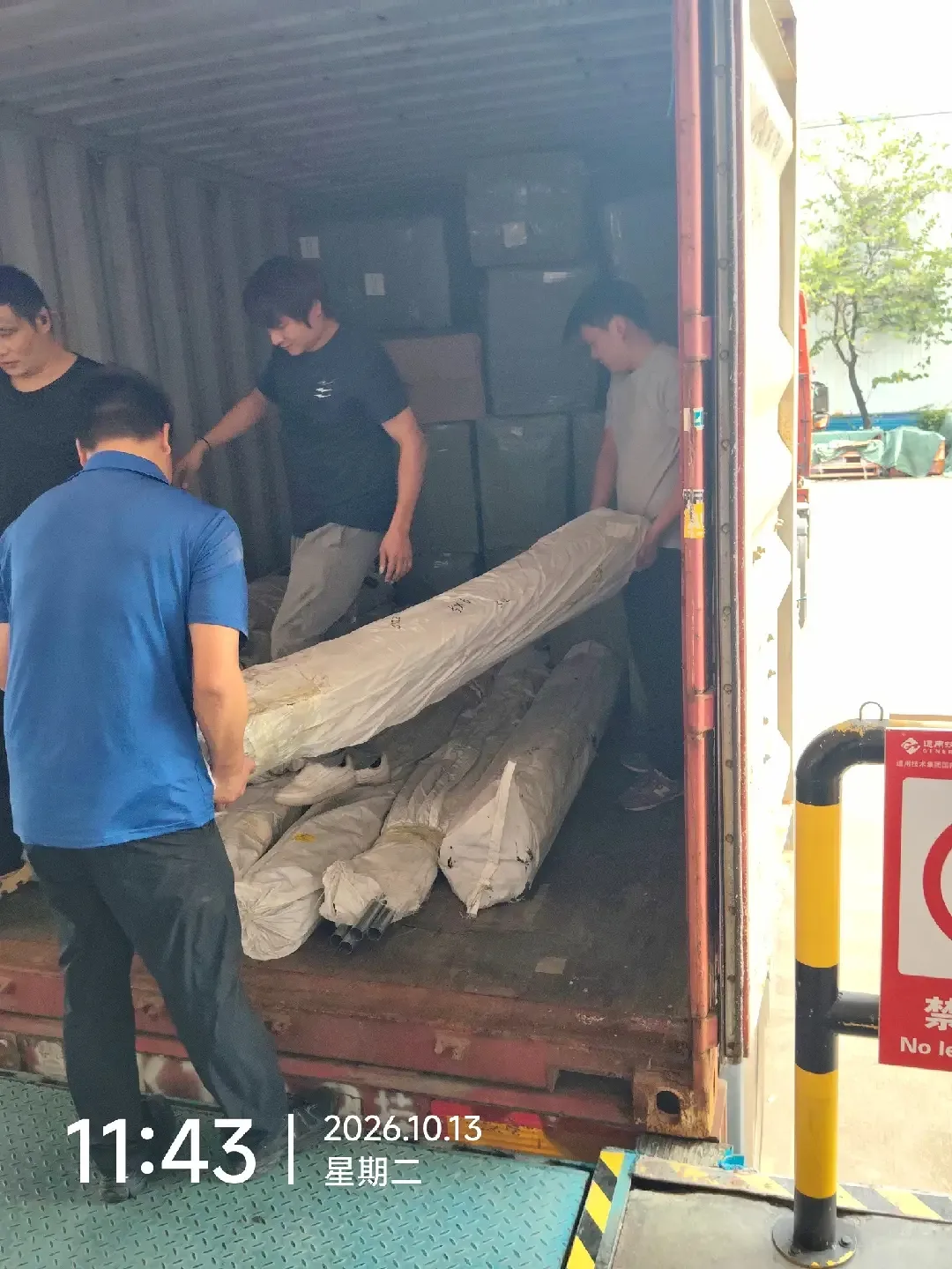 Workers handling wrapped tent supplies at the container entrance