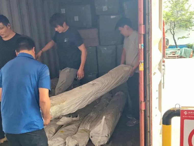 Workers carrying a long wrapped bundle into an open container